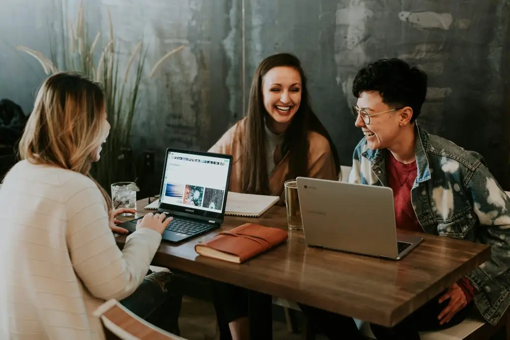 Three people in a coaching or mentoring session, sat a table with their lap tops