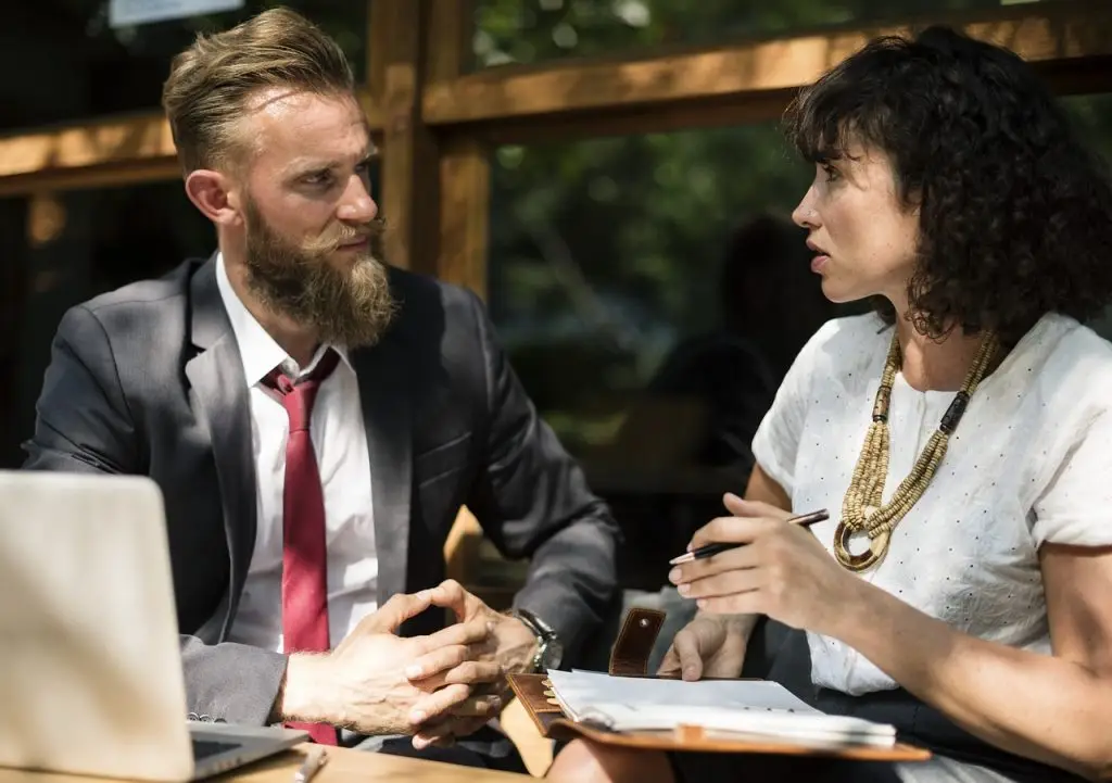 Man and a woman in deep conversation. The woman has an open notebook on her knee.