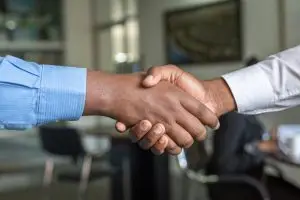 A picture of a handshake between a black man and a white man signifying agreement has been reached, in this case a successful job offer.